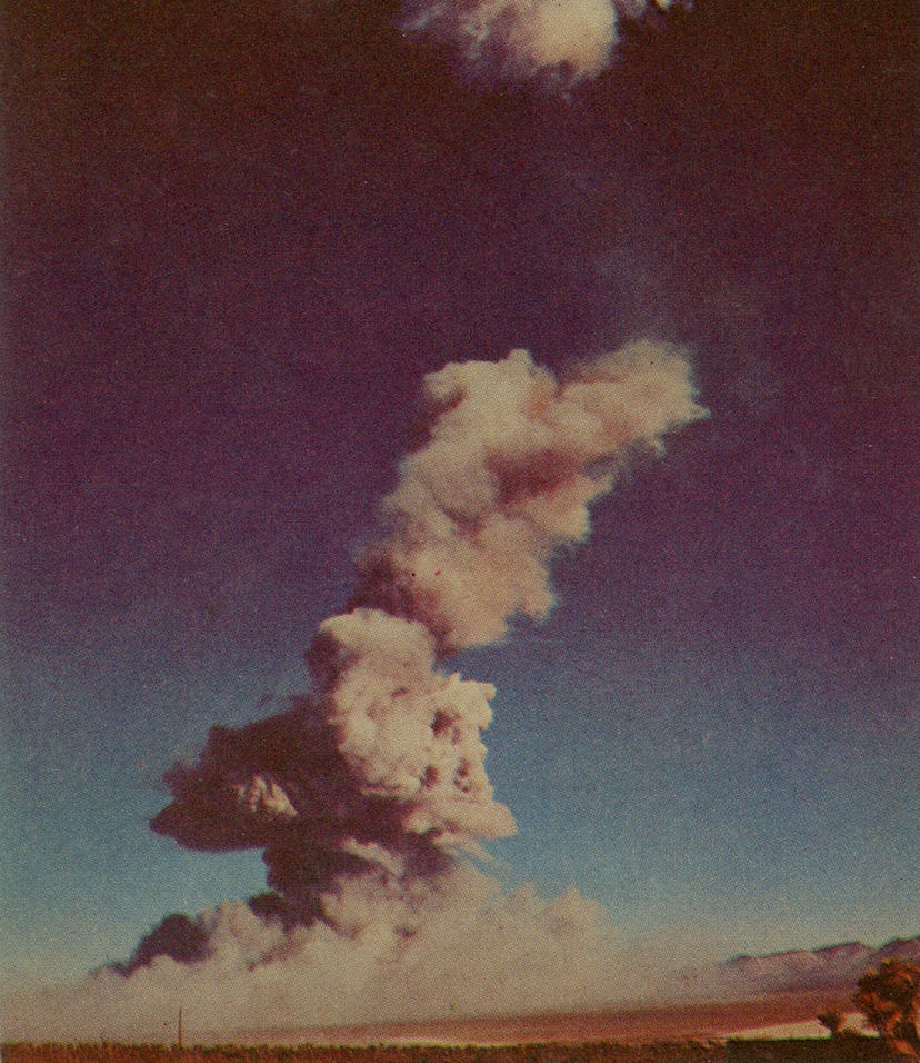 A photographic postcard shows an atomic cloud dissipating over an atomic detonation area, circa 1952...