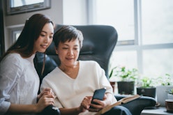 Asian mother and daughter having fun while using smartphone together at home