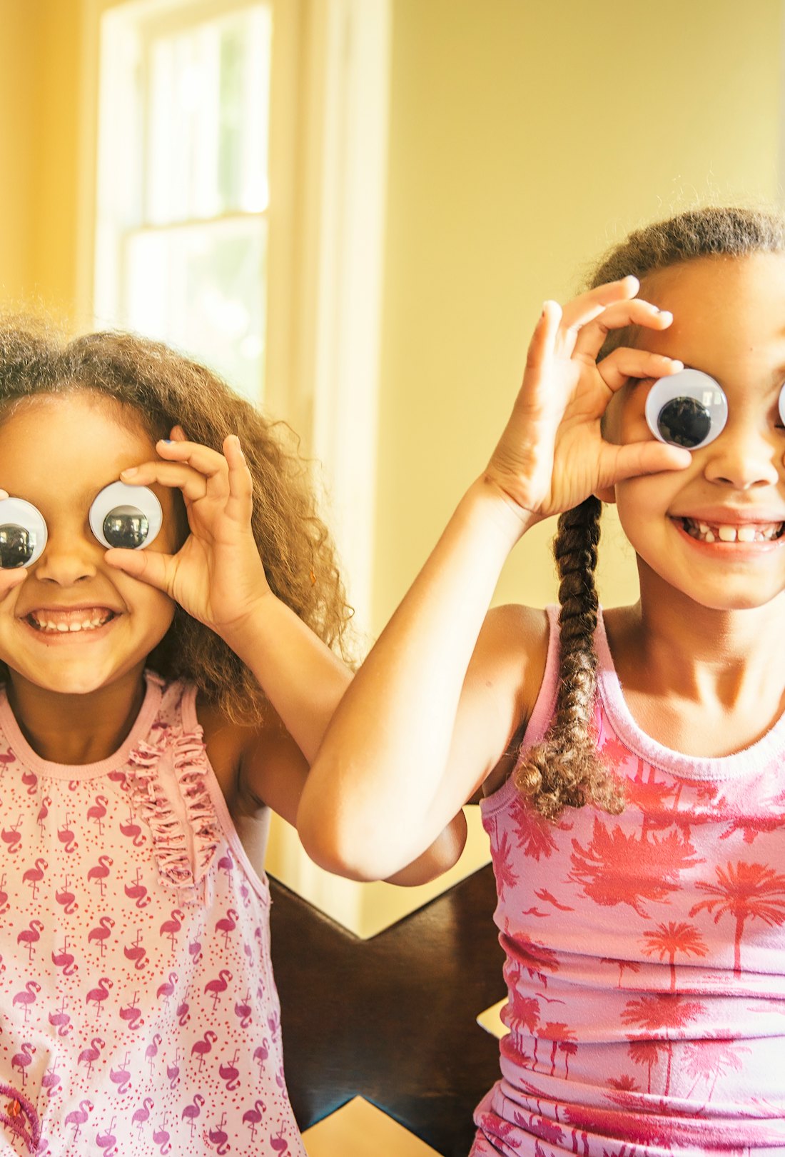 Two girls holding large googly eyes over their eyes and smiling