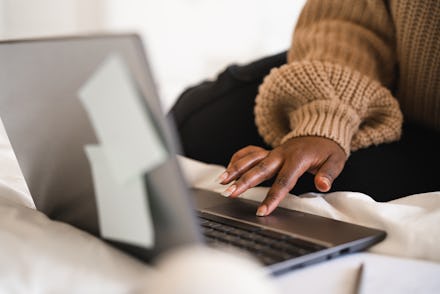 A female university student is sitting in her bed, studying on her laptop. She is working from home ...