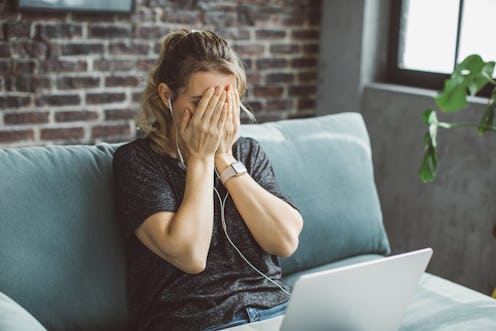 Mature woman having stressed video call on laptop while sitting on the sofa at home.