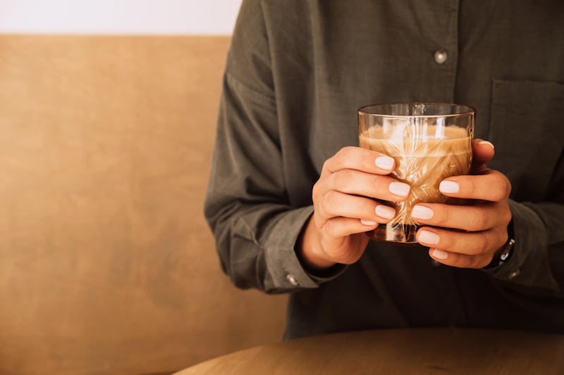 Photography of hands young female's in green linen blouse, holding the glass cup behind the wooden t...