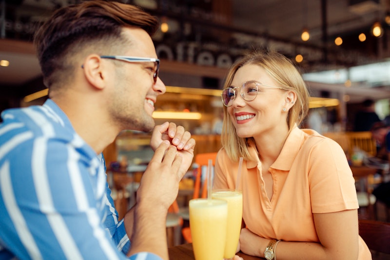 Happy Caucasian young couple having fun together, sitting in a coffee shop, smiling and enjoying the...