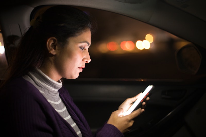 Woman text messaging using mobile phone in car at night