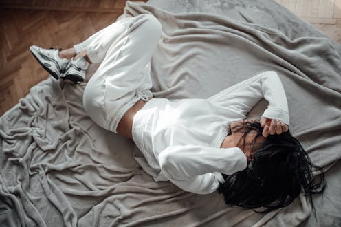 A woman lies on a bed in exhaustion. COVID vaccines can cause side effects including fatigue, fever,...