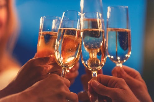 Group of friends toasting with champagne at night. They are standing outdoors in a restaurant at dus...