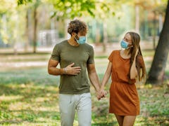 Portrait of Cheerful Young Couple with Face Masks who is Walking in the Park Path and Having a Nice ...