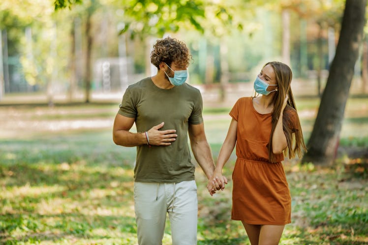 Portrait of Cheerful Young Couple with Face Masks who is Walking in the Park Path and Having a Nice ...