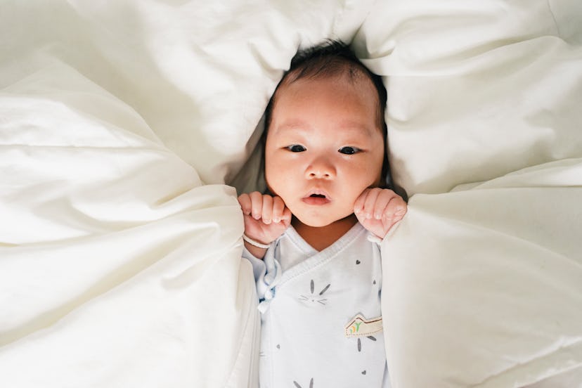 Baby on a bed, surrounded by pillows, in a story about May baby names.