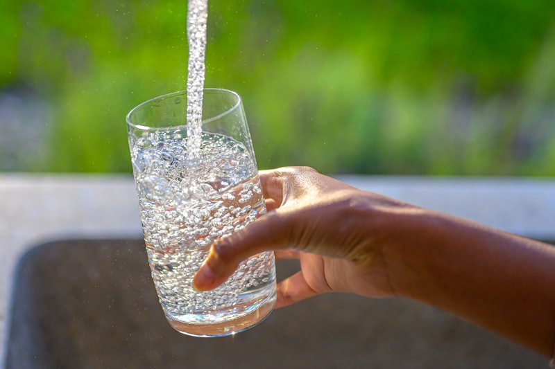Close-up of woman's hand filling glass with water in garden sink.