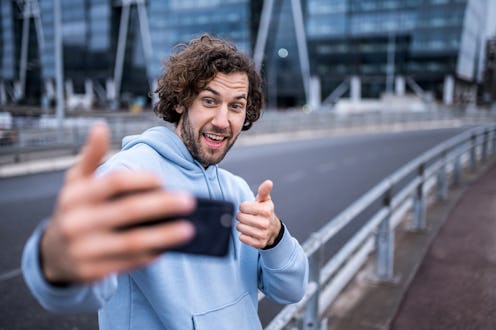 Happy young man running outdoors and taking a selfie in the city.