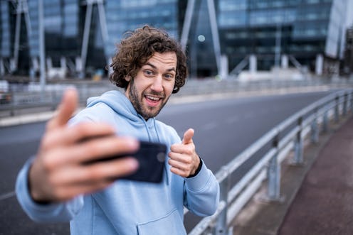 Happy young man running outdoors and taking a selfie in the city.