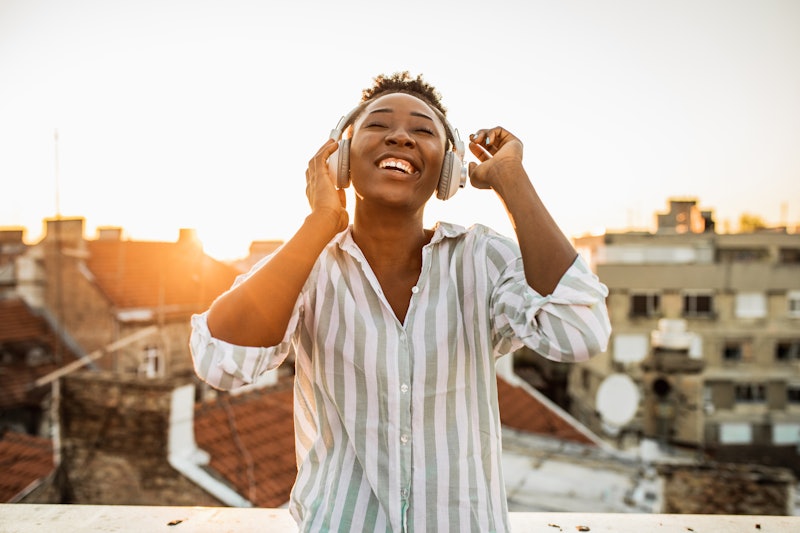 Photo of a young woman with headphones on the rooftop enjoying the sunset