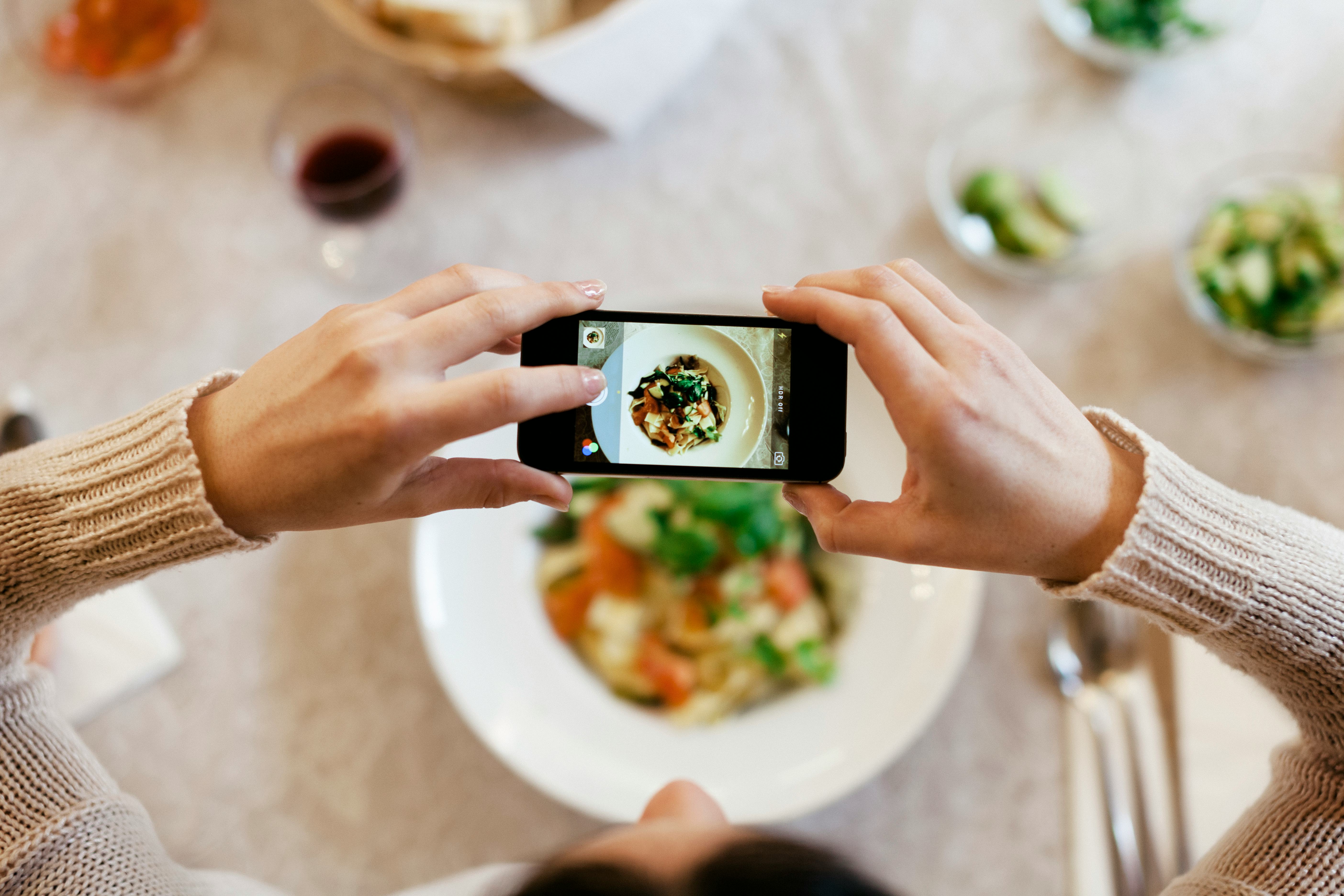 Bird's eye view of a woman taking a photo of her dinner with her smartphone. The plate is seen throu...
