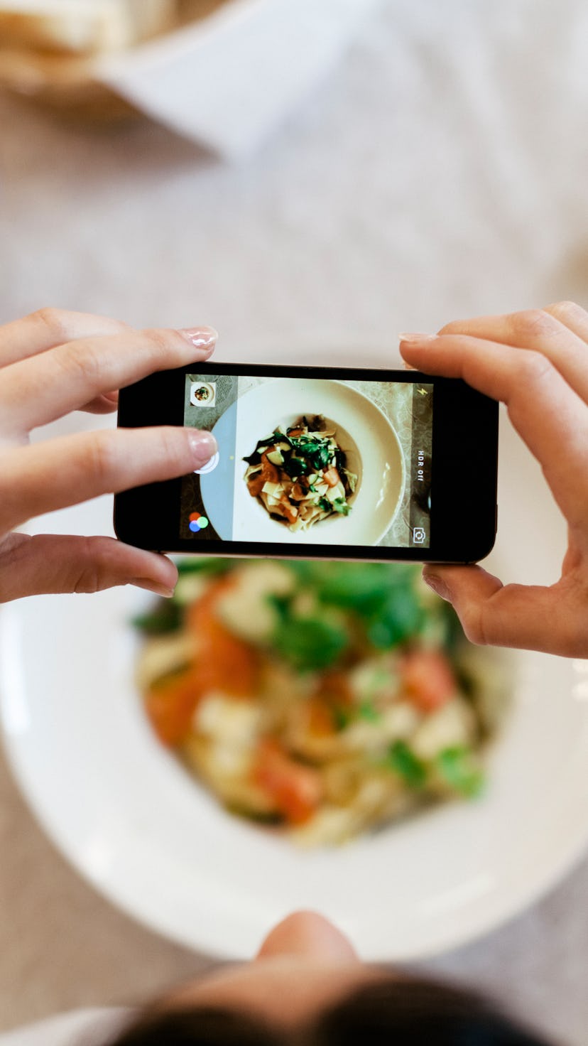 Bird's eye view of a woman taking a photo of her dinner with her smartphone. The plate is seen throu...