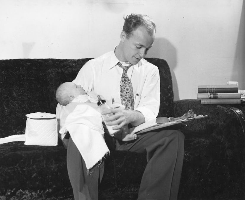 GI Bill student Roy Estes feeds his son, Larry Allan, a bottle as he studies for one of his Universi...
