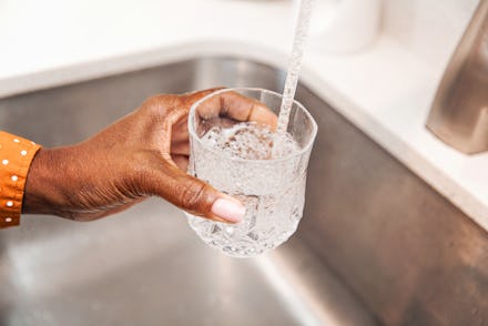Unrecognizable woman pouring herself a glass of tap water from the kitchen sink