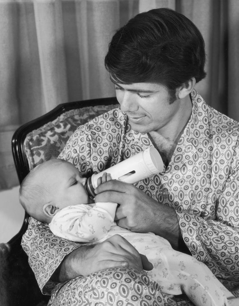 circa 1965:  A man wearing patterned pajamas sits and feeds a baby with a bottle.  (Photo by Lambert...