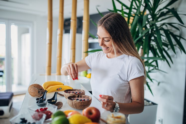 A woman prepares a fruit ice cream bowl at home in her kitchen.