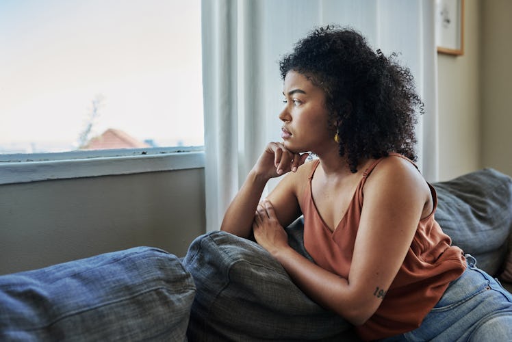 Shot of a young woman looking pensively out a window at home