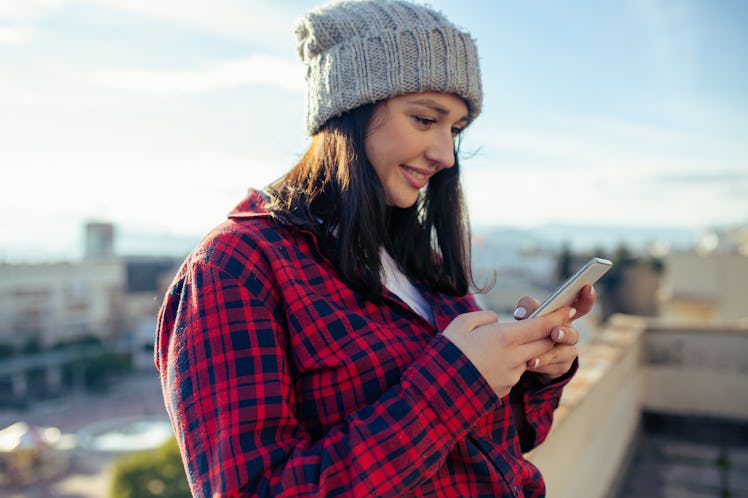 Young woman using smart phone while enjoying sunny day on rooftop.