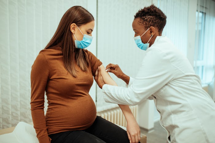 African American female doctor preparing a pregnant woman for vaccination. Pregnant woman getting a ...