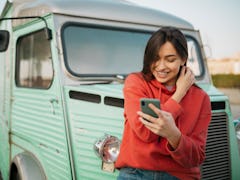 Happy young Caucasian woman standing outdoors, in front of an old truck and in a red shirt, smiling ...