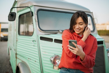 Happy young Caucasian woman standing outdoors, in front of an old truck and in a red shirt, smiling ...
