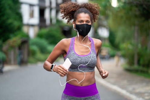 A person wearing a gray and purple sports bra, headphones, and a mask runs outside. As long as you'r...