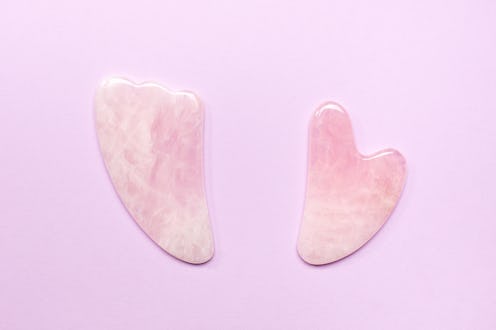 Top view of pink jade scraping tools for gua sha procedure placed on lilac background