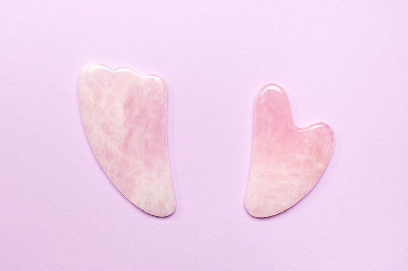 Top view of pink jade scraping tools for gua sha procedure placed on lilac background