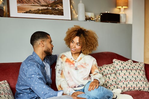Girlfriend looking at boyfriend talking while sitting on sofa. Young man and woman are discussing in...