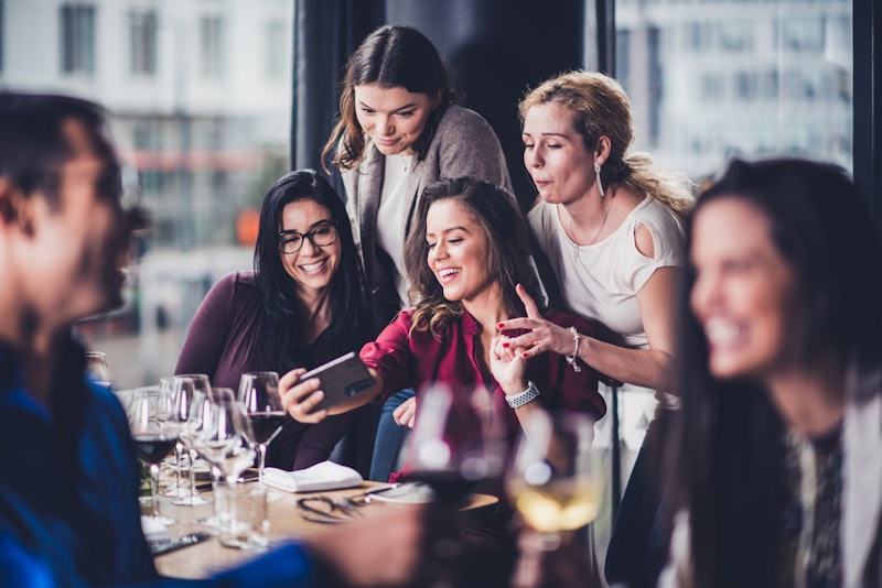 Young friends taking selfies at a restaurant. Here's how to rebuild your social interaction skills a...