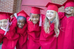Adorable kindergarten graduates smile and pose for photo together outside preschool