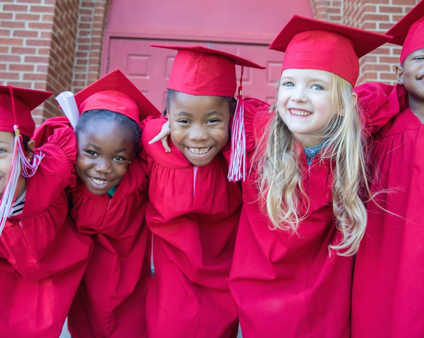 Adorable kindergarten graduates smile and pose for photo together outside preschool