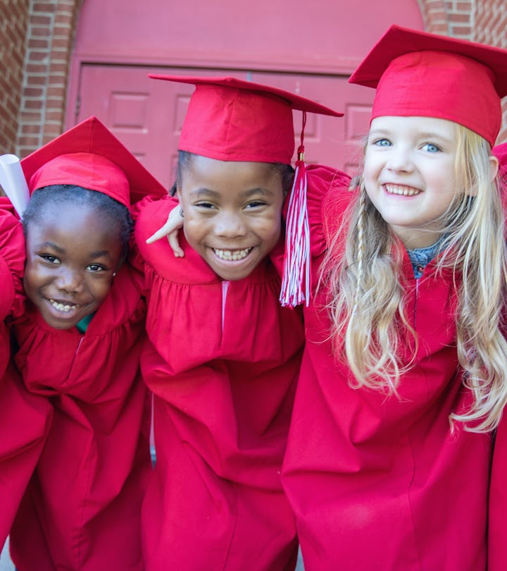 Adorable kindergarten graduates smile and pose for photo together outside preschool