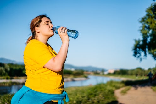 Oversized young Caucasian woman drinking water after running in a public park.