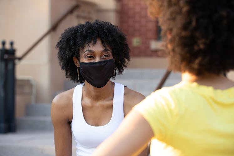 Young adult woman sitting on steps and wearing a mask while talking to friend