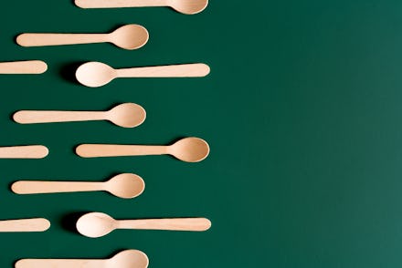 Layout of wooden disposable teaspoons on a dark green emeral background. Zero waste recyclable conce...