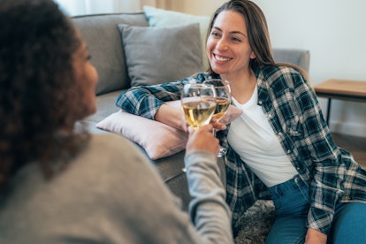 Two female friends making small talk together and drinking wine while sitting at home