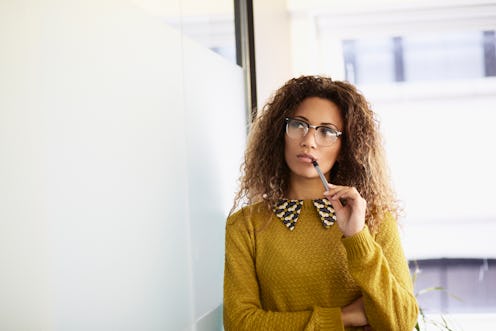 office woman thinking while holding pen against her mouth 