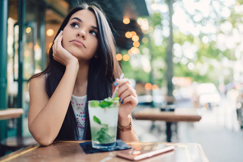 Thoughtful woman at sidewalk cafe drinking cold cocktails