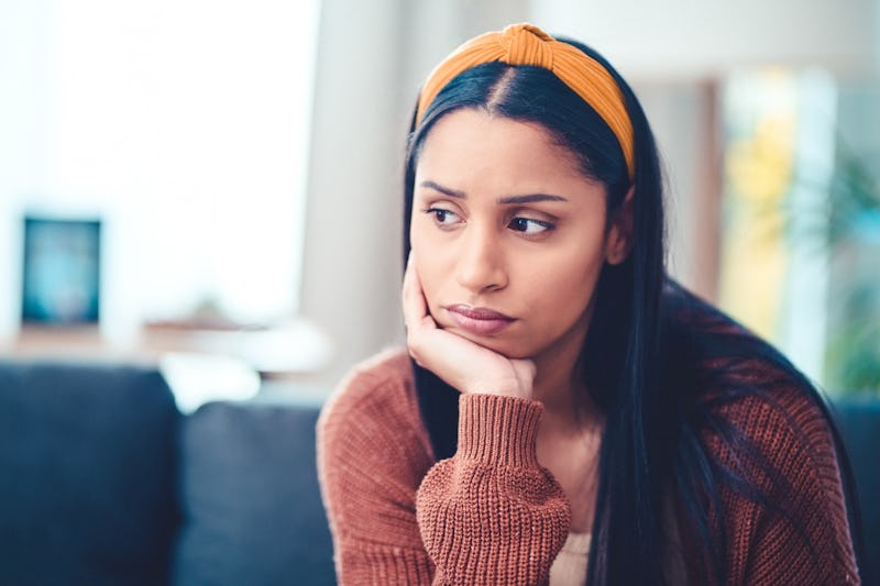 Shot of a young woman looking unhappy on the sofa at home