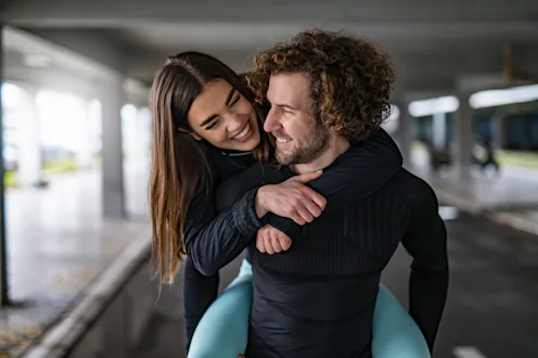 Playful young athletic couple having fun. Young man carrying his girlfriend and embracing. They are ...