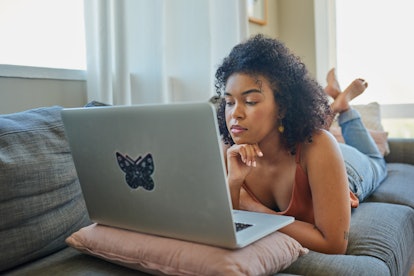 Shot of a young woman using a laptop while relaxing on a sofa at home