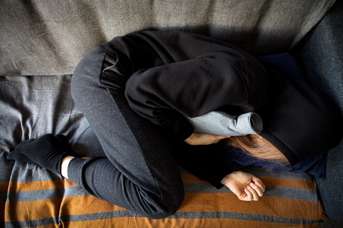 High angle shot of a woman experiencing stomach pain and holding a hot water bottle lying on the sof...