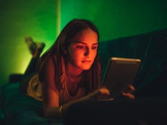 Sad young Caucasian cute woman using tablet at night. Chatting, reading or watching movie.