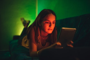 Sad young Caucasian cute woman using tablet at night. Chatting, reading or watching movie.