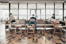 Businesspeople working and maintaining social distance on a sofa in a modern office