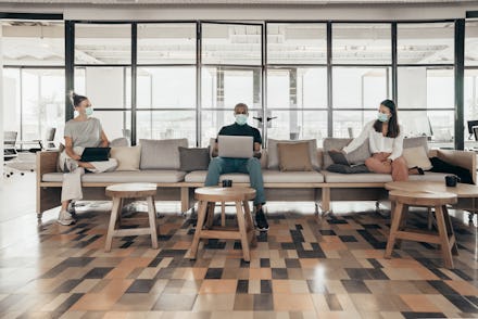 Businesspeople working and maintaining social distance on a sofa in a modern office